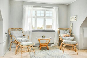Ein Zimmer mit zwei Korbstühlen, einem kleinen runden Tisch und einem Fenster mit weißen Vorhängen.