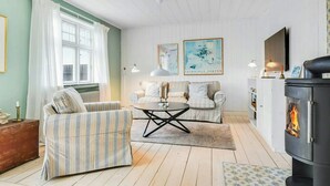 Een zithoek met gestreepte banken, een ronde salontafel, een open haard en twee ingelijste kunstwerken.