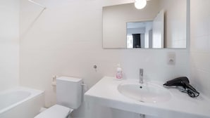 Casa de banho com lavatório branco, espelho e sanita.