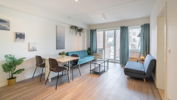 Uma sala de estar moderna com um sofá, uma mesa de jantar com cadeiras, uma mesa de centro e uma janela grande com cortinas.