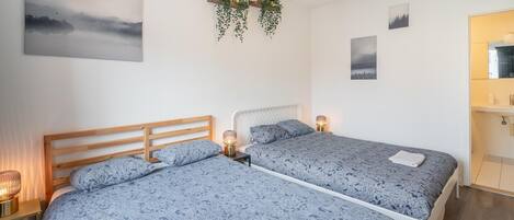 A room with two beds, a wooden headboard, bedside lamps, and wall-mounted greenery.