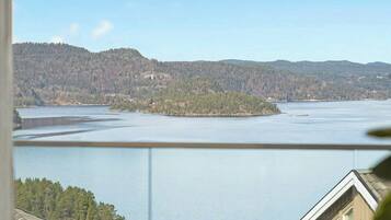 Ein See mit bewaldeten Hügeln im Hintergrund, ein Haus mit Balkon und einem klaren Himmel.