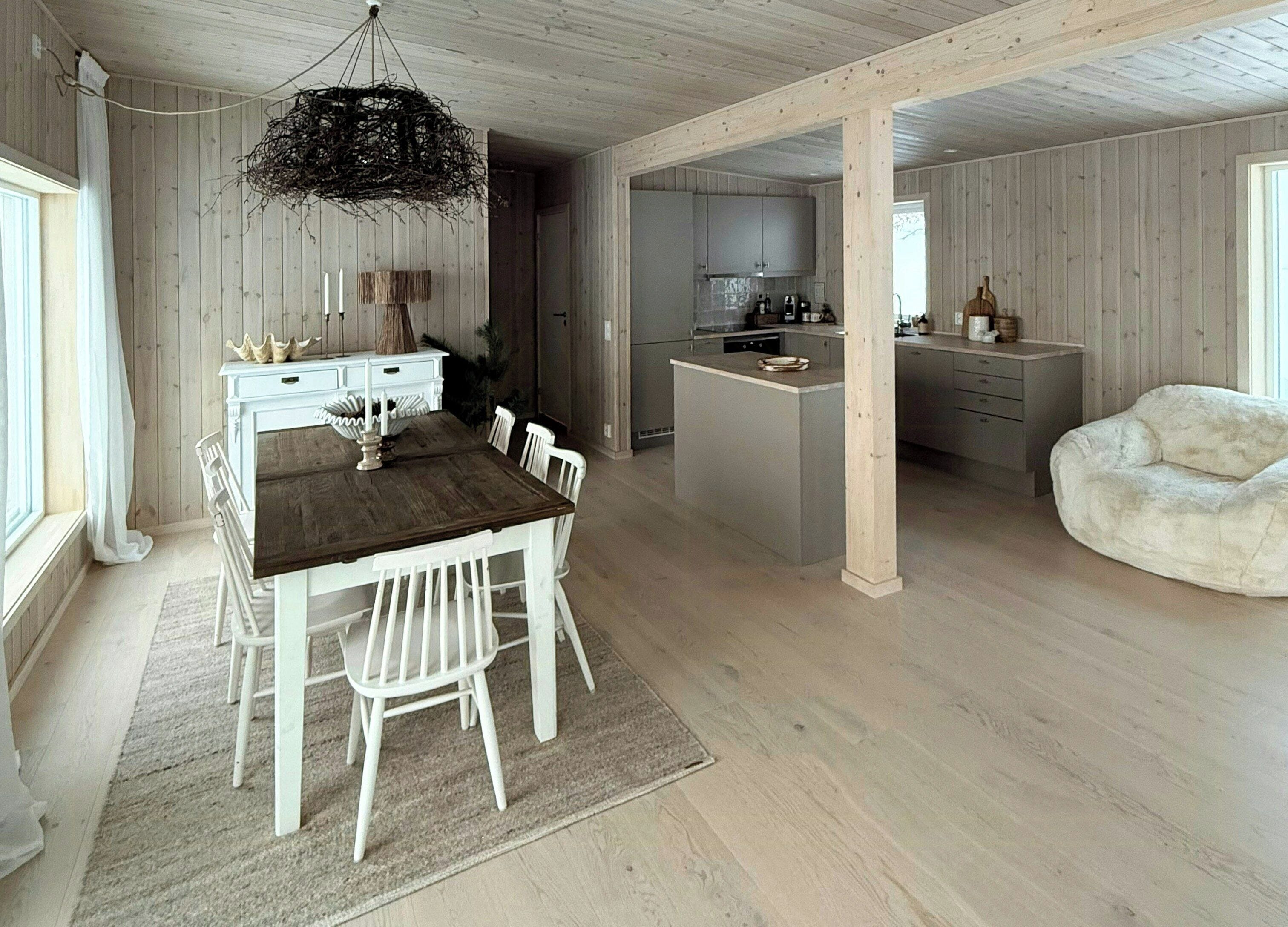 Ein geräumiger Raum mit einem Holztisch, weißen Stühlen, einer Pendelleuchte und einer Küchenzeile mit Schränken und einer Arbeitsplatte.