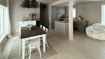 Ein geräumiger Raum mit einem Holztisch, weißen Stühlen, einer Pendelleuchte und einer Küchenzeile mit Schränken und einer Arbeitsplatte.