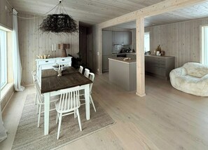 A spacious room with a wooden dining table, white chairs, a hanging light fixture, and a kitchen area with cabinets and a countertop. - Modern cabin with panoramic views near Kragerø (Stabbestad)