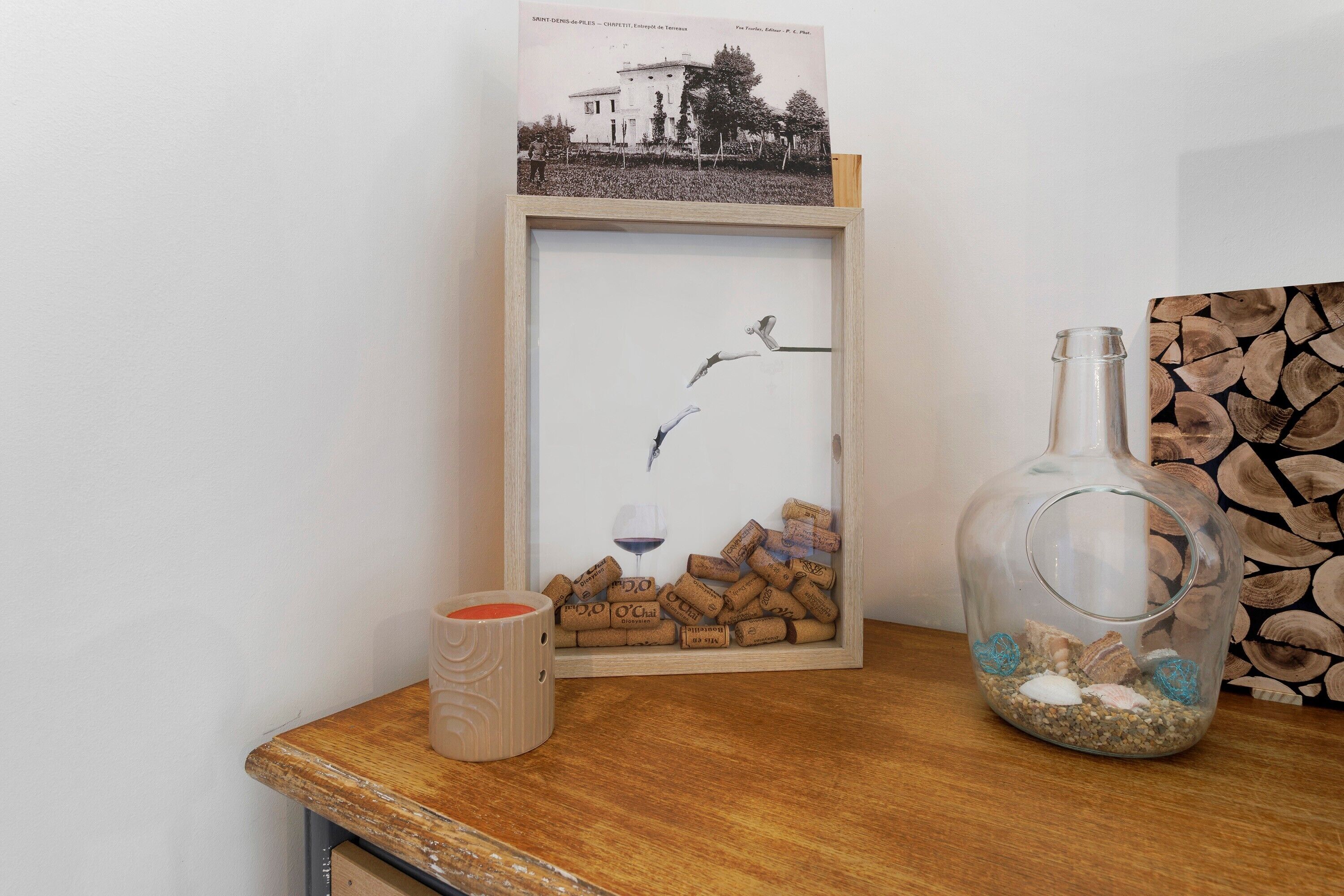 Fotograma con un pájaro volando sobre corchos de vino, una botella de vidrio y una taza sobre una mesa de madera.