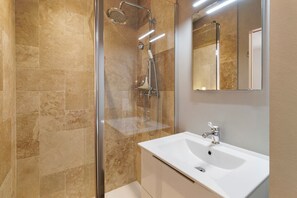 Ein modernes Badezimmer mit einer Duschkabine, einem weißen Waschbecken und einem Spiegel.