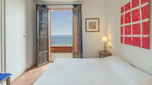 A bedroom with a large bed, an open door leading to a balcony with a view of the sea, and a red abstract painting on the wall. - Villa with Pool and Spectacular Sea Views (Begur)
