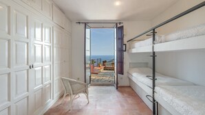 A room with bunk beds, a wicker chair, and a view of the sea through an open door. - Villa with Pool and Spectacular Sea Views (Begur)