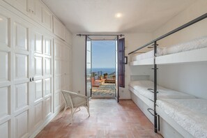 Una habitació amb llits superposats, una cadira de vimet i vista al mar per una porta oberta.