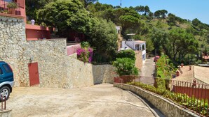 A stone-walled building with a red door, a blue car parked in front, and a view of a hillside with trees and a clear sky. - Villa with Pool and Spectacular Sea Views (Begur)