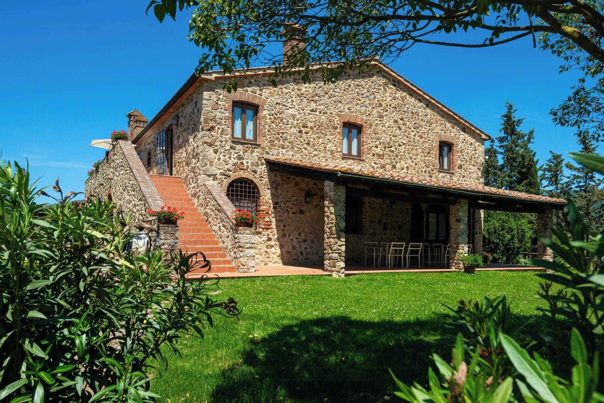 Une maison en pierre dotée d’un patio couvert, d’un escalier et d’une pelouse bien entretenue.