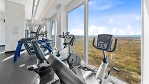 A gym with cardio machines, large windows, and a view of the outdoors. - Stunning Gulf Front Views | Beach Access | Indoor & Outdoor Pools (Gulf Shores)