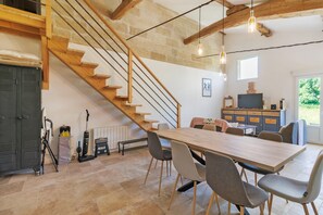 Ein geräumiges Zimmer mit einer Holztreppe, einem Esstisch mit Stühlen, einem Fernseher und einem Fenster mit Blick ins Grüne.