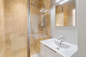 Ein modernes Badezimmer mit einer Duschkabine aus Glas, einem weißen Waschbecken und einem Spiegel darüber.