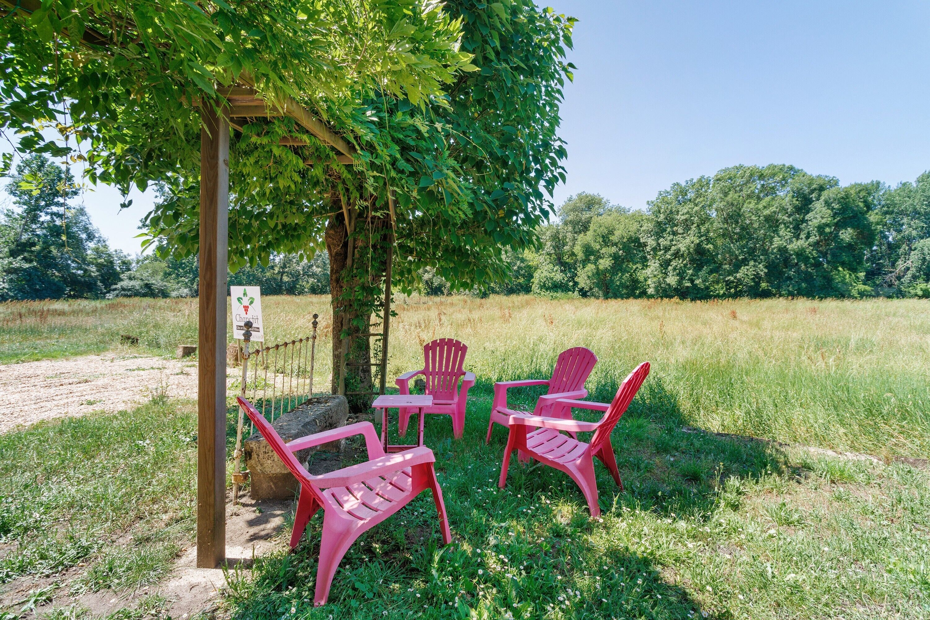 Een prieel met een bordje, omringd door rode plastic stoelen en een tafel in een grasveld.