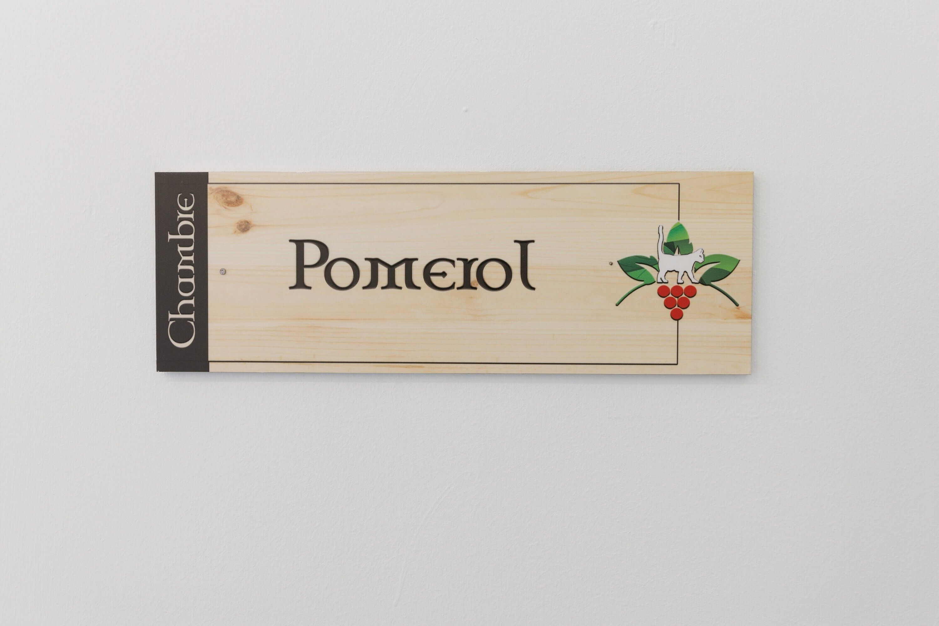 Une enseigne en bois portant le nom « Pomerol » et un logo représentant un chat et des raisins.