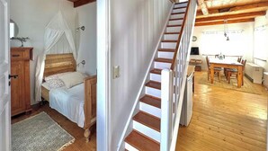 Een slaapkamer met een houten bed, nachtkastje, en een raam met een witte gordijn.