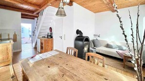 Een houten eettafel met stoelen, een bank, een open haard en een trap naar een hoger gelegen verdieping.