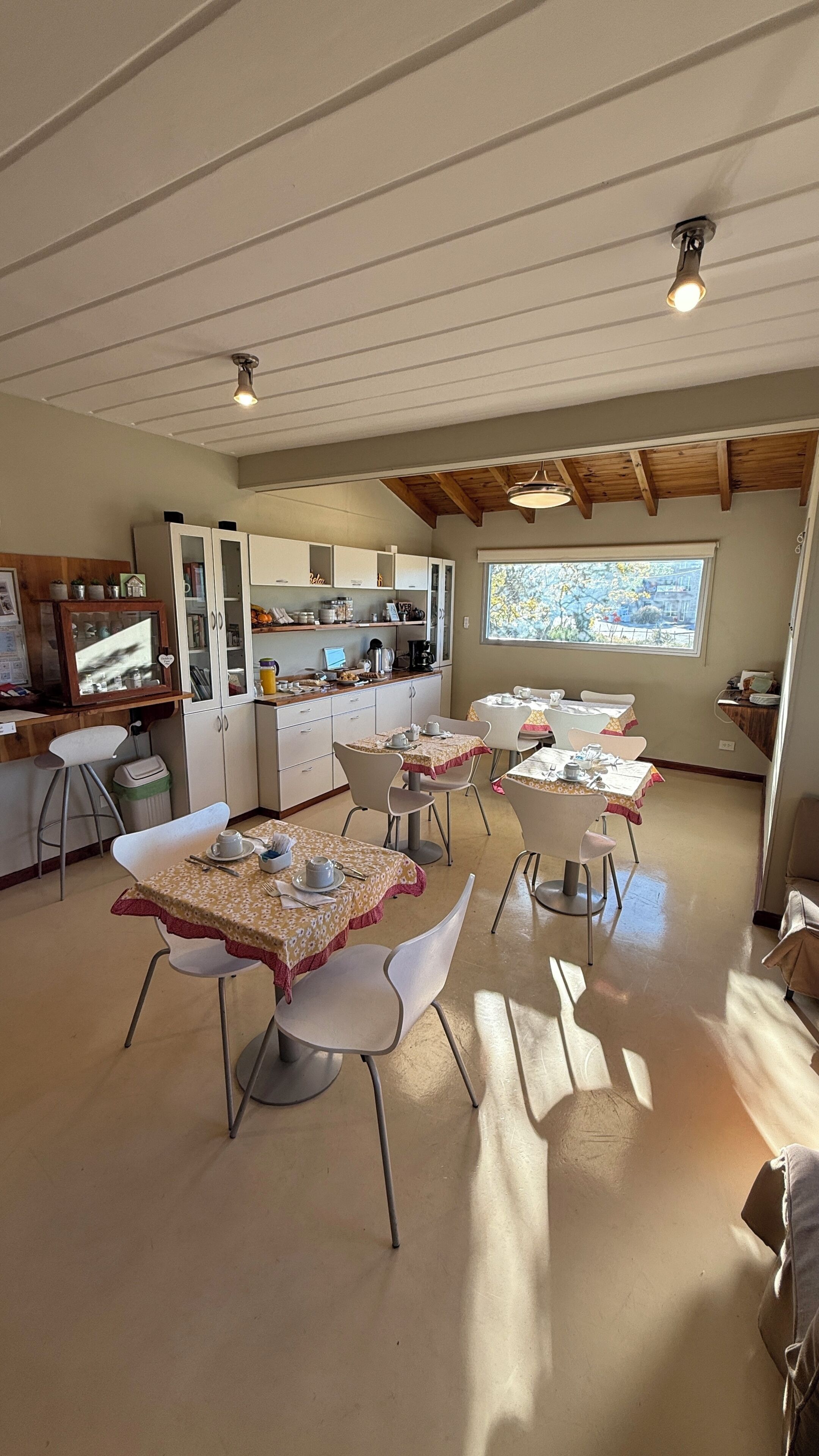 A dining area with tables and chairs, a kitchen area with cabinets and appliances, and a view through a window.