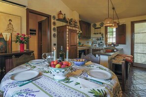Un'area pranzo con tavolo apparecchiato per quattro, una cucina sullo sfondo e un tavolo da pranzo con tovaglia floreale.