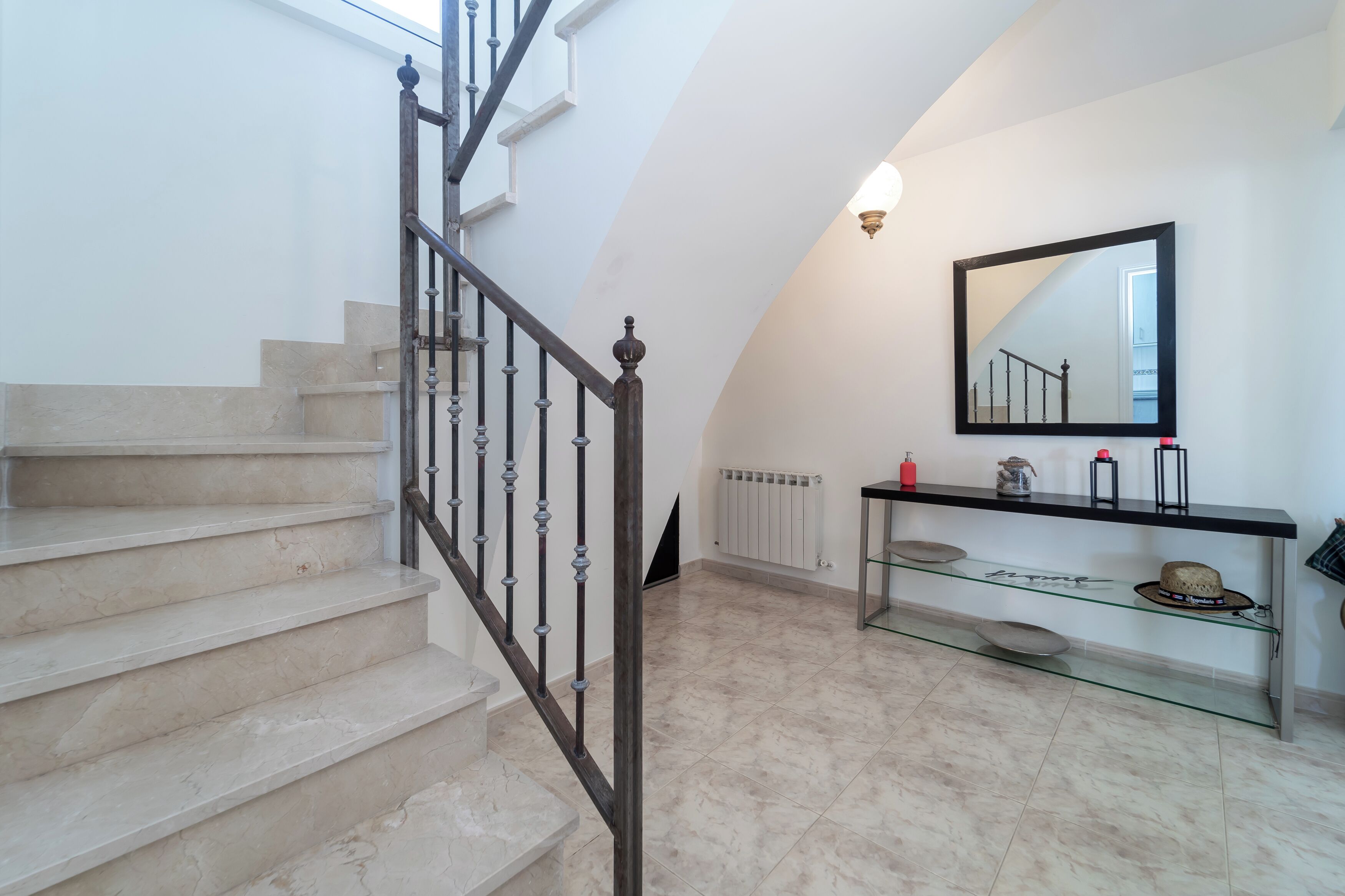 A staircase with a metal railing, a glass console table with a mirror, and a radiator on the wall.