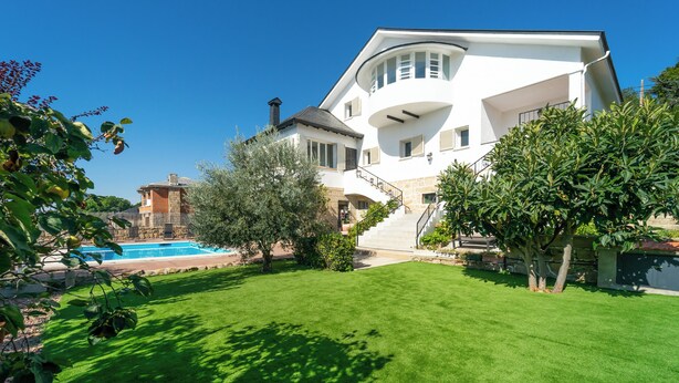 A large white house with a swimming pool, a well-maintained lawn, and a staircase leading to the entrance.