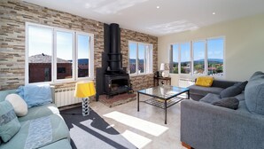A living room with a fireplace, large windows, and a view of the landscape.