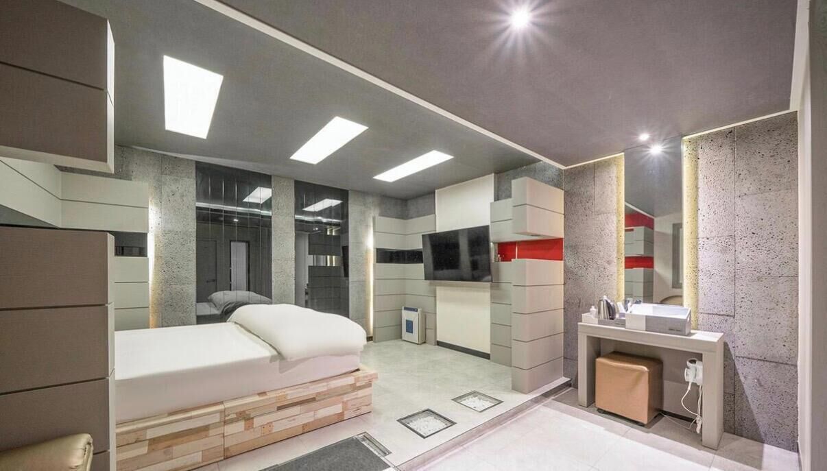 Un dormitorio moderno con cama, una kitchenette pequeña, un baño con espejo y una televisión.