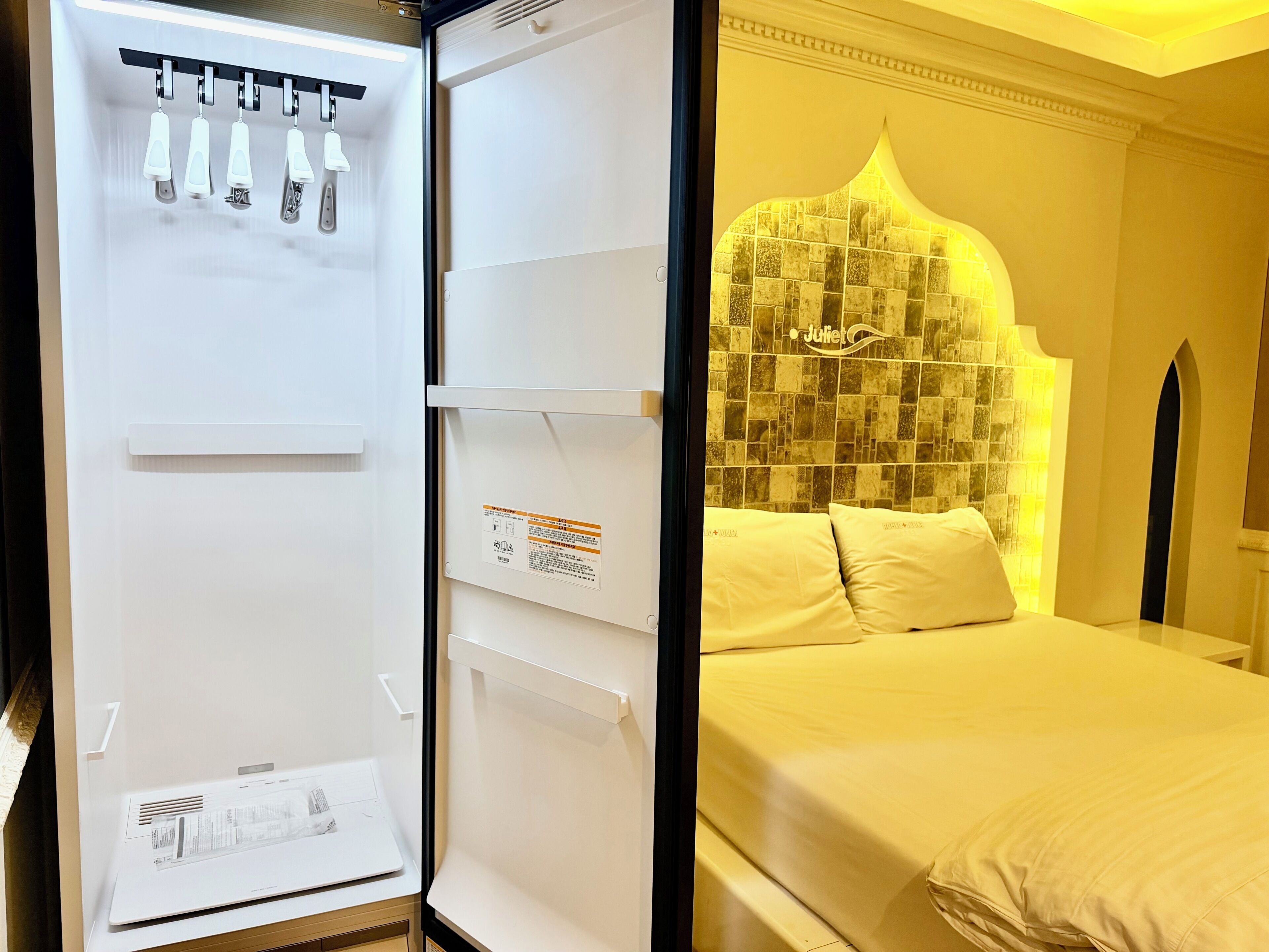 Una habitación de hotel con cama, pared blanca y cabecera de cama con azulejos.