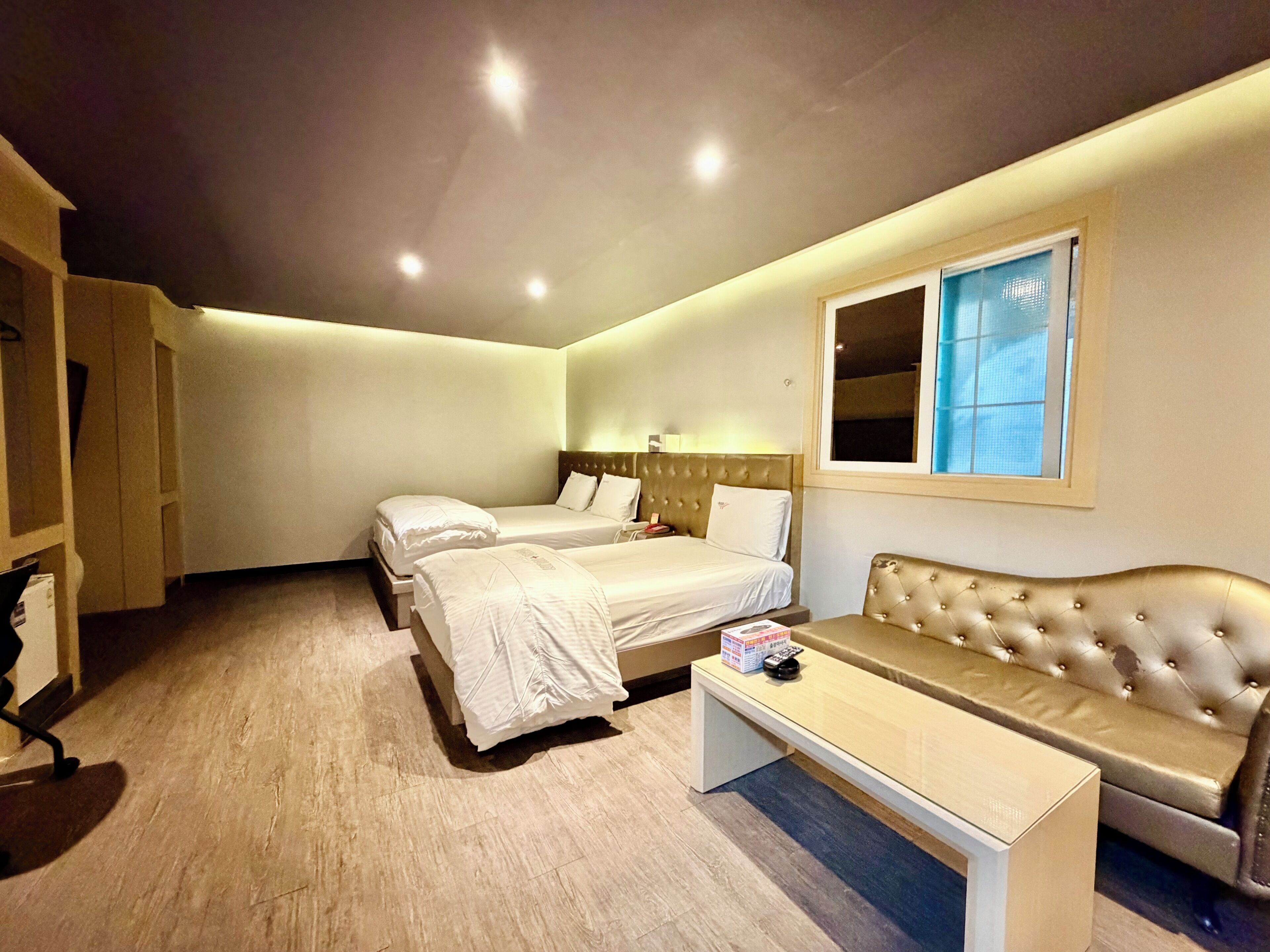 Quarto de hotel com duas camas, um sofá, uma mesinha e uma janela.