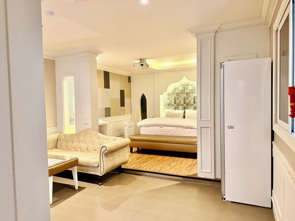 A hotel room with a bed, a sofa, a small table, a mirror, and a door.