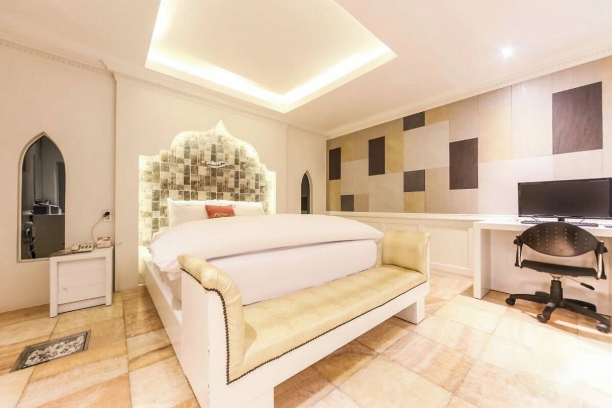 A bedroom with a bed, a desk, a chair, and a television.