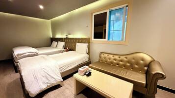 A hotel room with two beds, a sofa, a small table, and a window.