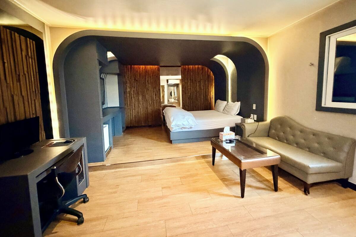A hotel room with a bed, a sofa, a desk, and a television.