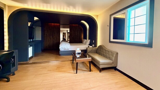 Una habitación de hotel con cama, sofá, mesita, televisor y ventana con persianas.