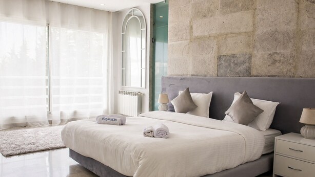 Quarto moderno com uma cama grande, uma mesa de cabeceira, uma luminária e vista para o exterior pela janela.