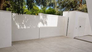 Um espaço exterior limpo e moderno, com uma parede branca, um portão de rolo fechado e chão em mosaico.