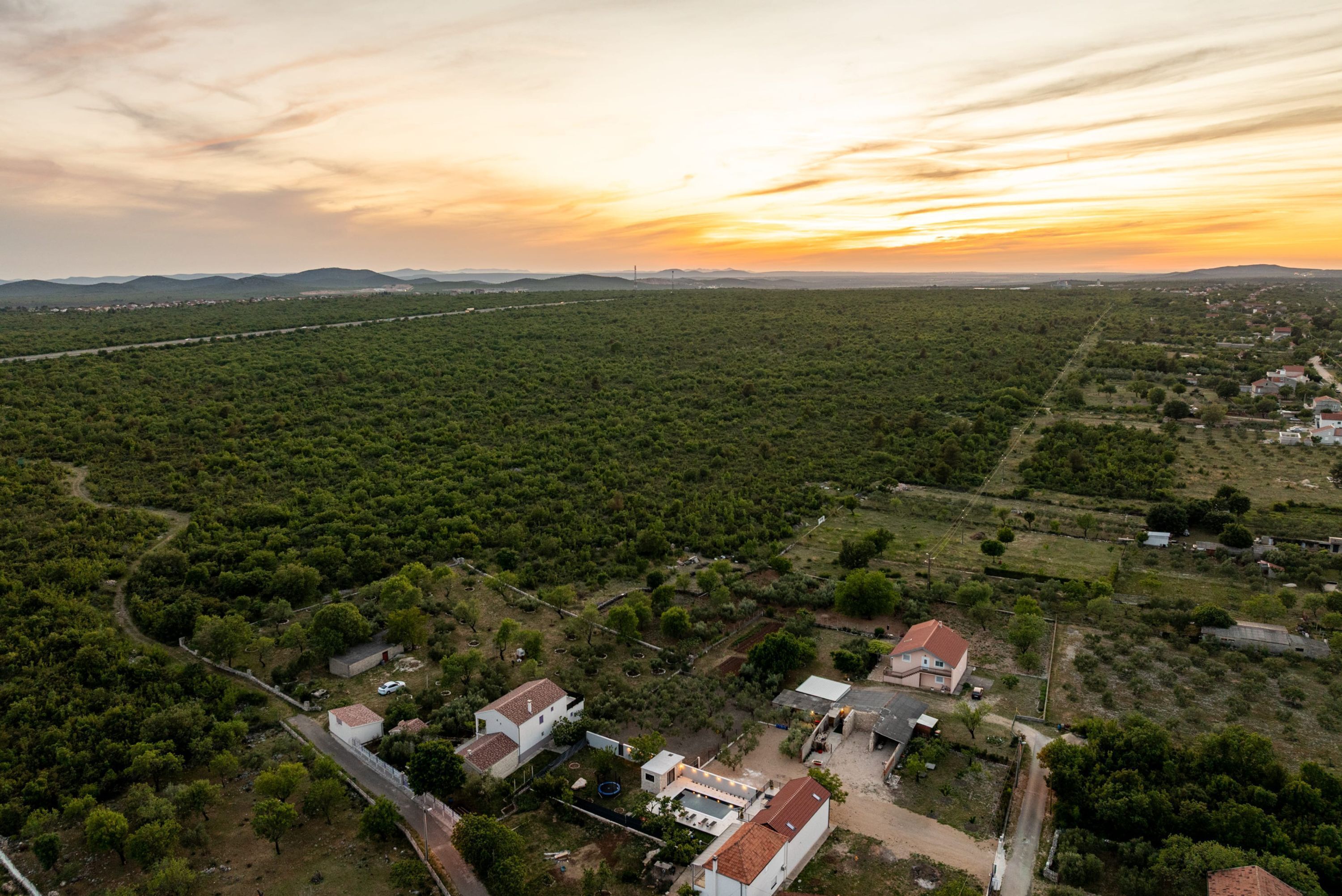 An aerial view of a rural area with scattered houses, roads, and a clear sky.
