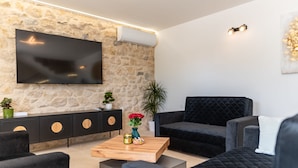 A modern living room with a stone wall, a flat-screen TV, a black sofa, a wooden coffee table, and a black console with circular doors. - Villa Flora Zadar Villas (Benkovac)