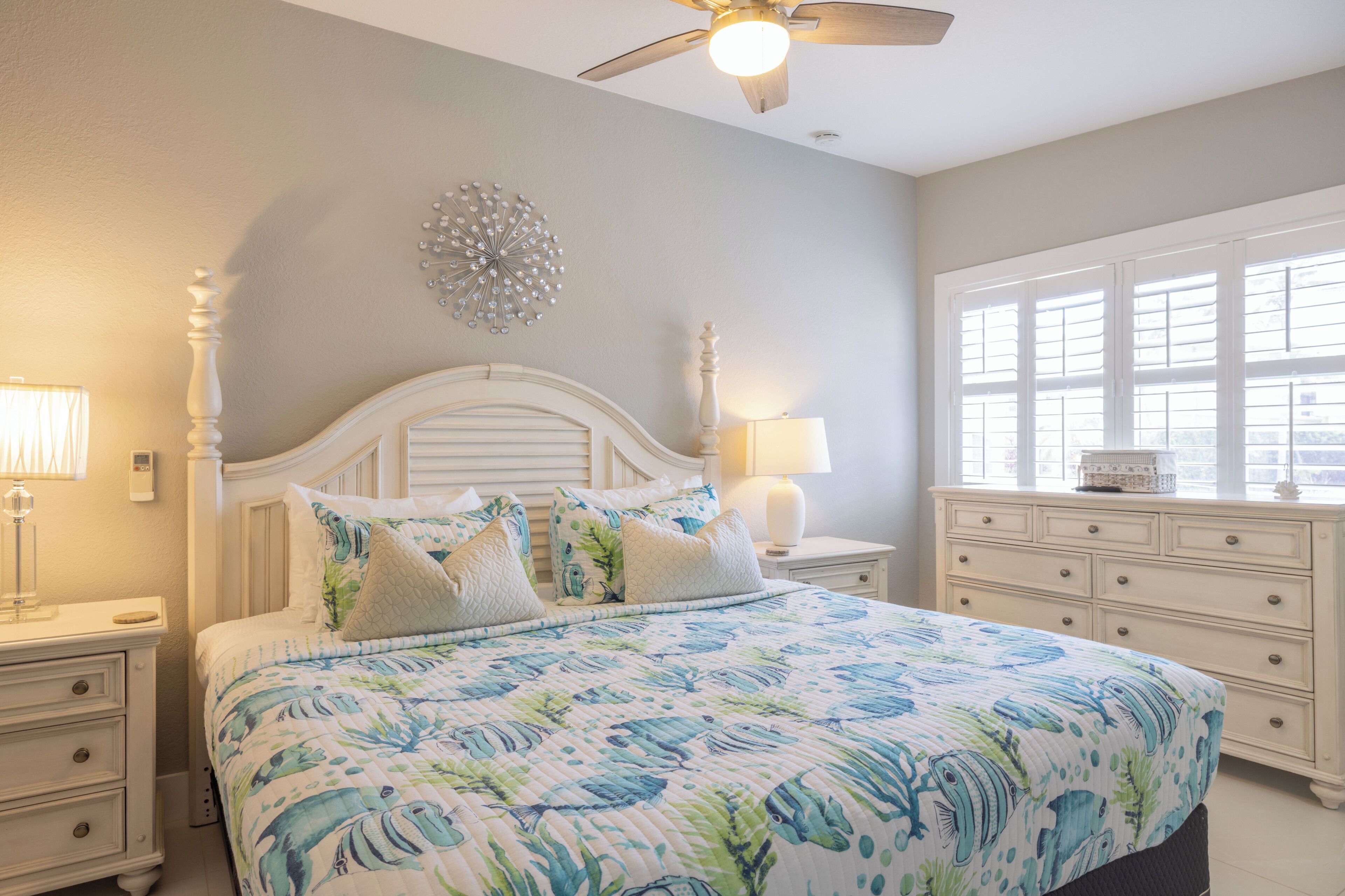 A bedroom with a bed, nightstands, a dresser, a ceiling fan, and a window.