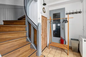 A staircase with wooden steps and a metal handrail, a coat rack with clothes, a fire extinguisher, and a radiator.