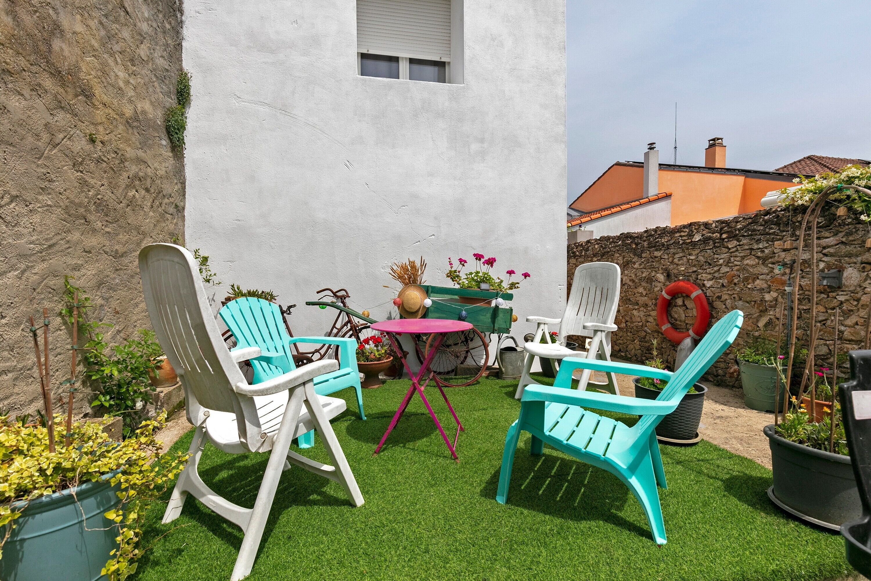 Une terrasse avec un revêtement de gazon synthétique, des chaises blanches et turquoise, une petite table ronde et des plantes en pot.