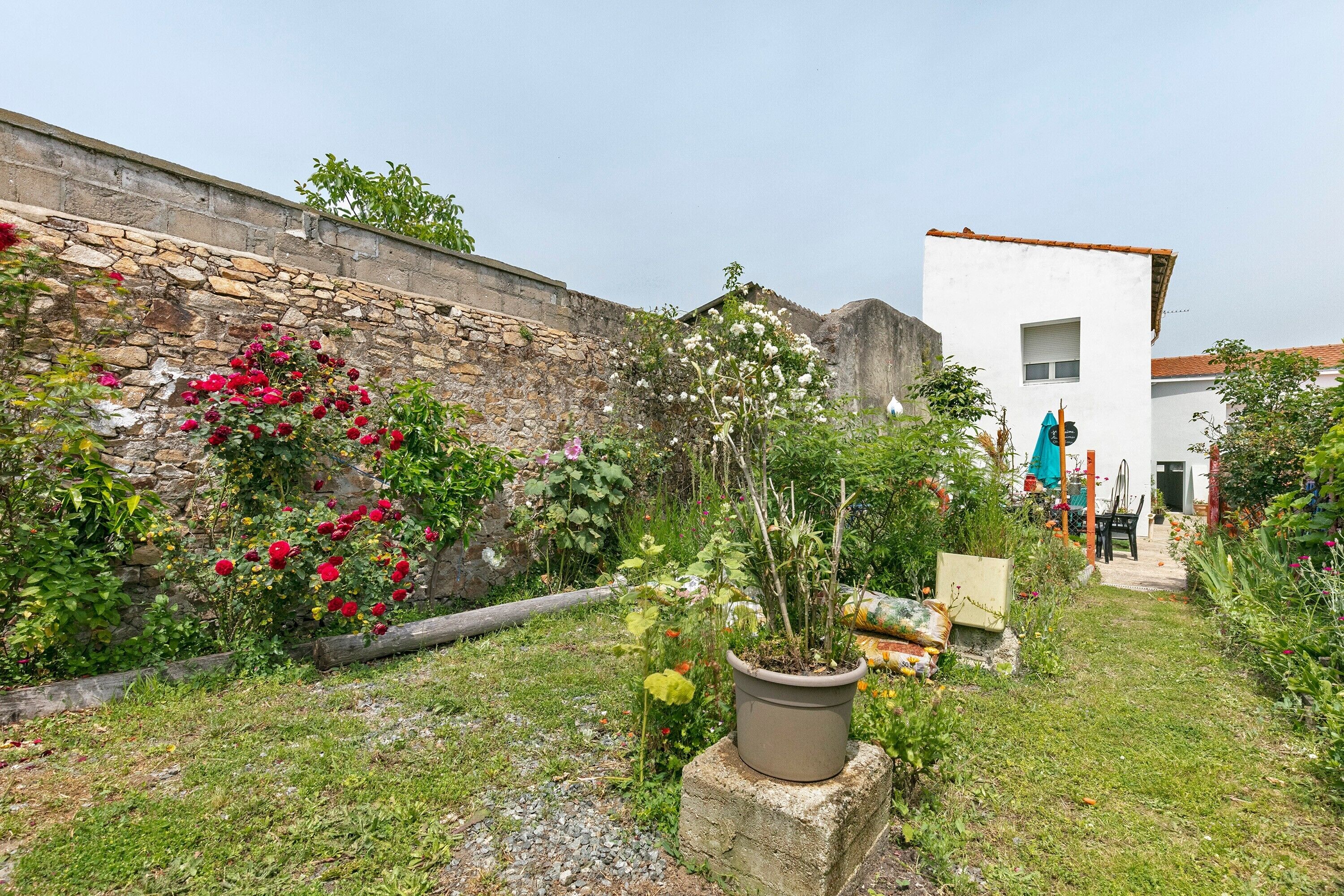 Un jardí amb una paret de pedra, plantes en testos i un edifici blanc amb una finestra.