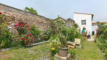 A garden with a stone wall, potted plants, and a white building with a window.