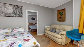 A bedroom with a bed, a sofa, a chair, a painting, and a wall hanging.