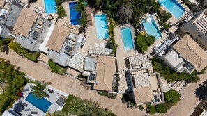 Eine Vogelperspektive eines Resorts mit mehreren Schwimmbecken, Liegestühlen und einer gepflegten Landschaft.