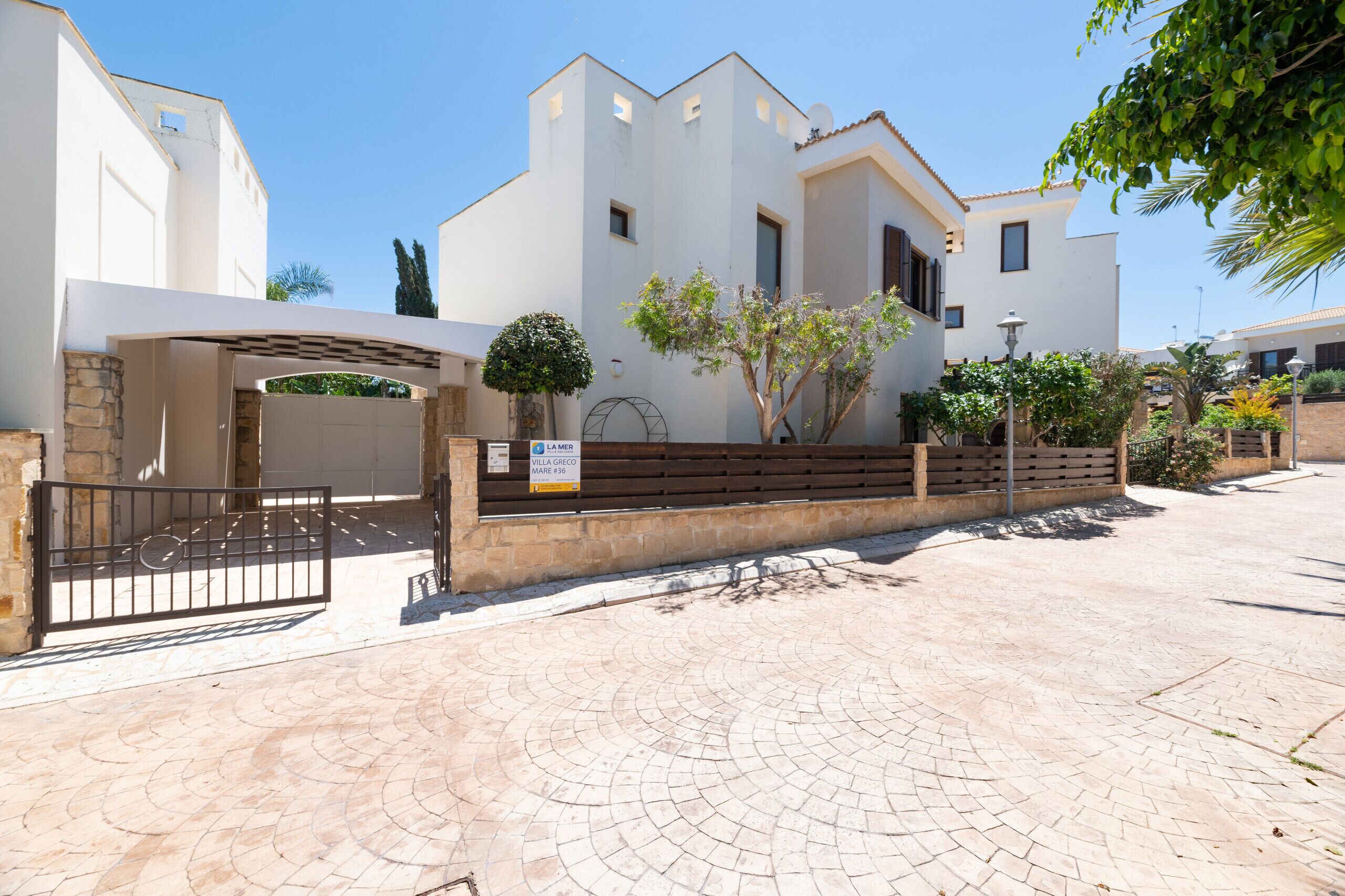 Eine moderne Villa mit gepflasterter Auffahrt, einem verschlossenen Eingang und einem Schild mit der Aufschrift 'Villa Greco'.