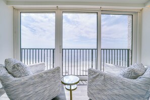 Ein Balkon mit zwei gestreiften Sesseln und einem kleinen runden Tisch, mit Blick auf einen Strand und einer Geländer.