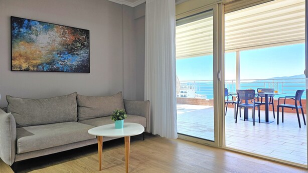 A modern living room with a sofa, a small table, and a view of the sea through a sliding glass door. - Deep Blue Rooftop - 111 (Sarandë)